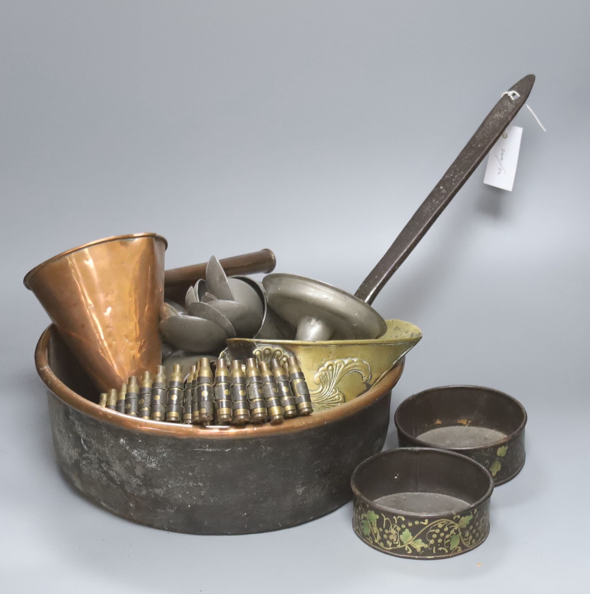 A group of assorted metalware including a copper pan, a brass stirrup, a pewter mug filled with pewter spoons, and a pair of toleware coasters